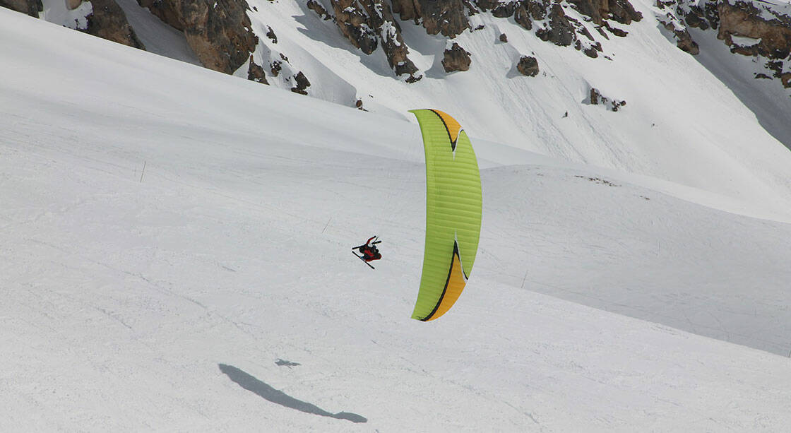 individu survolant les montagnes enneigées en parapente et skis aux pieds