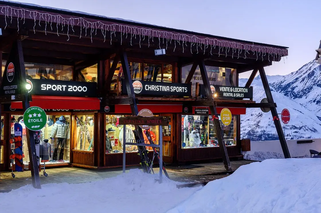 Gevel van de winkel Sport 2000 Christina Sports in Arc 1600, verlichte etalages in de sneeuw bij schemering