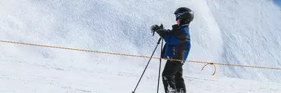 garçon sur piste de ski avec ses bâtons un casque et un masque