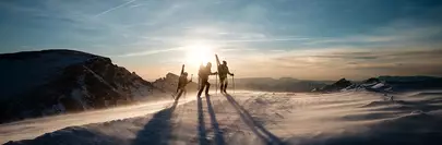 3 randonneurs portant leurs skis sur le dos