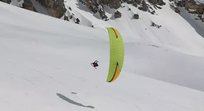 individu survolant les montagnes enneigées en parapente et skis aux pieds