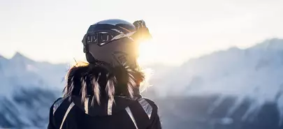 vue de dos d'une femme face à la montagne, qui porte un casque de ski