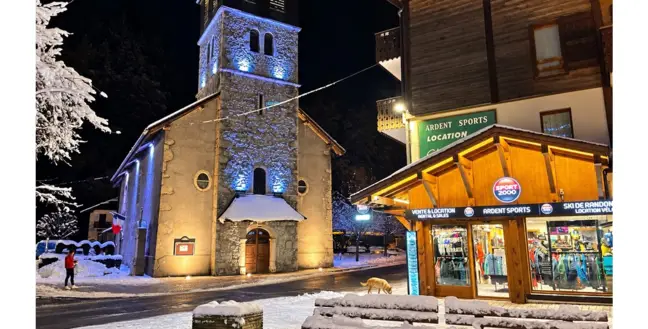 Le magasin Ardent Sports éclairé le soir, à côté de l'église de Montriond
